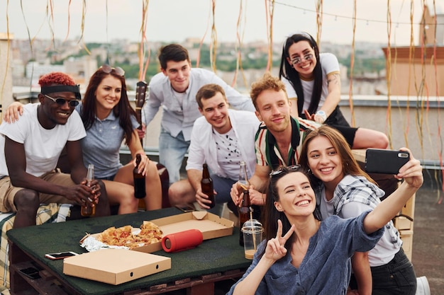 Girl making selfie With delicious pizza Group of young people in casual clothes have a party at rooftop together at daytime