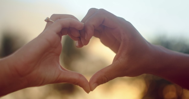 Foto ragazza che fa il simbolo dell'amore con le sue mani contro il meraviglioso cielo dorato e il sorgere del sole mattutino