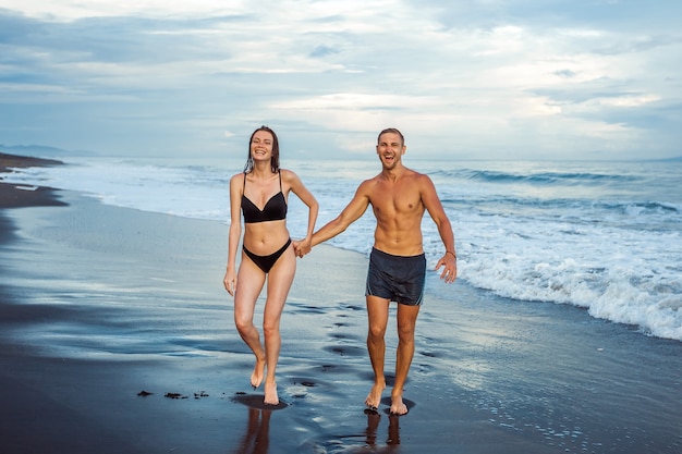 The girl and the man walk on the beach in swimsuits