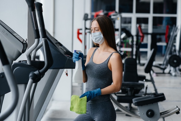 Photo the girl in the mask disinfecting the gym equipment during a pandemic.