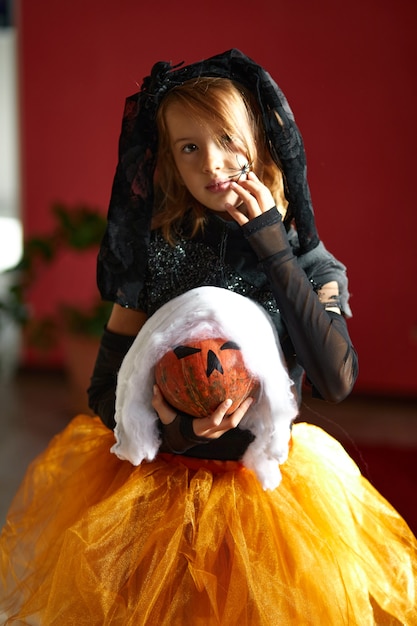 Girl in mask at home in halloween costume with pumpkin Jack or Laurent