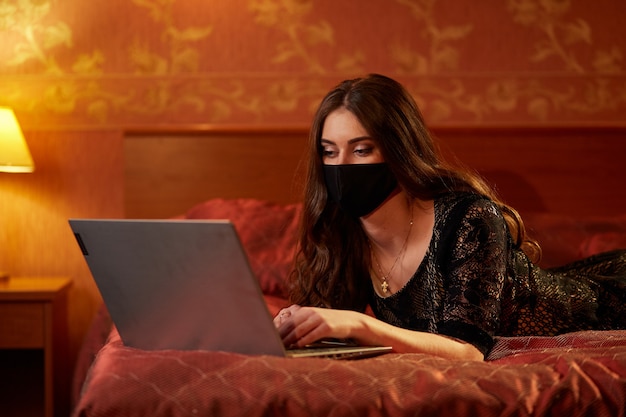 The girl in the mask with a laptop on the bed