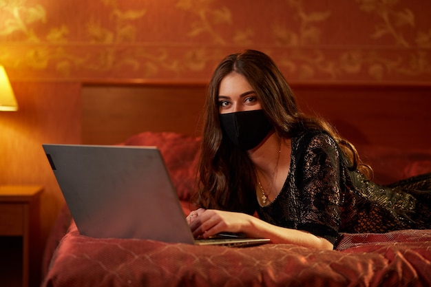 The girl in the mask with a laptop on the bed
