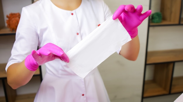 Foto una ragazza, una maestra dell'epilazione allo zucchero, si trova di fronte a un cliente con una veste bianca e guanti rosa