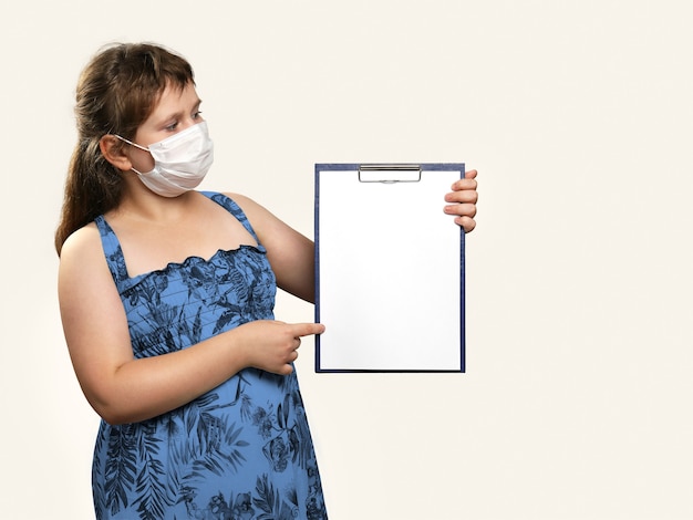 Girl in medical face mask holds clipboard in her hands and shows something on it