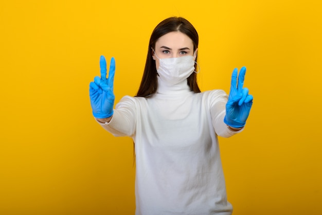 Девушка в медицинских перчатках одевает медицинскую маску на лице на заднем плане. Респираторная инфекция. COVID-19