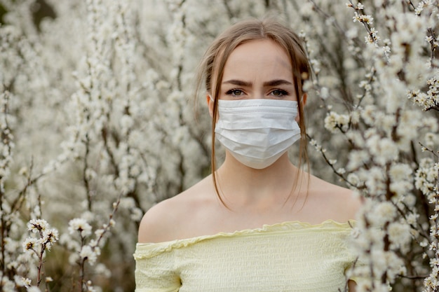 Ragazza in una mascherina medica. ragazza in primavera tra il giardino fiorito. una ragazza in una mascherina medica protettiva. concetto di allergia di primavera