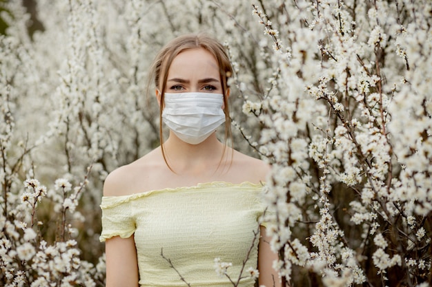 Девушка в медицинской маске. Девушка весной среди цветущего сада. Девушка в защитной медицинской маске. Концепция весенней аллергии