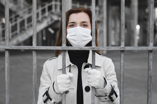 Foto la ragazza con la mascherina medica è isolata per strada e tiene in mano un recinto. coronavirus. covid19