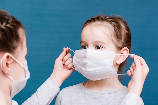 A girl in a medical mask puts a clean mask on another girl. Child protection