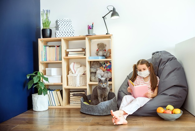 Photo a girl in medical mask siting on wood floor and reading a books during quarantine