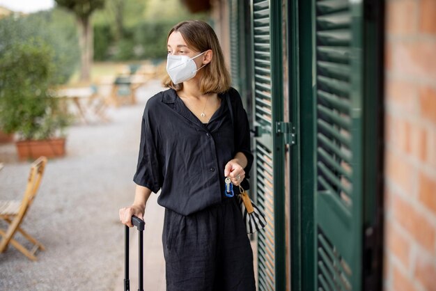 La ragazza in maschera medica con bagaglio va in camera d'albergo