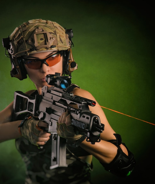 The girl in military overalls airsoft posing with a gun in his hands on a dark background