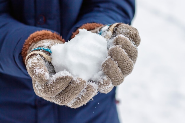 ミトンの女の子が雪玉を持っています。晴れた冬の日に雪玉を遊ぶ_