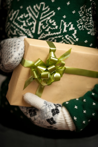 Девушка в варежках и свитер с зимним орнаментом держит рождественские подарки