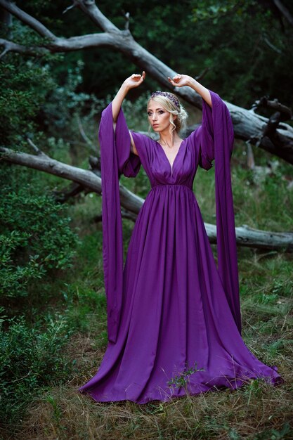 Girl model blonde in a lilac dress with a bouquet with a green forest