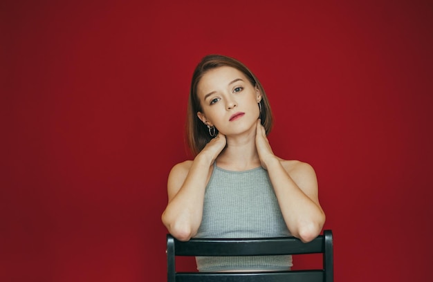 Girl model in casual clothes sits on a chair on a red background and poses at the camera