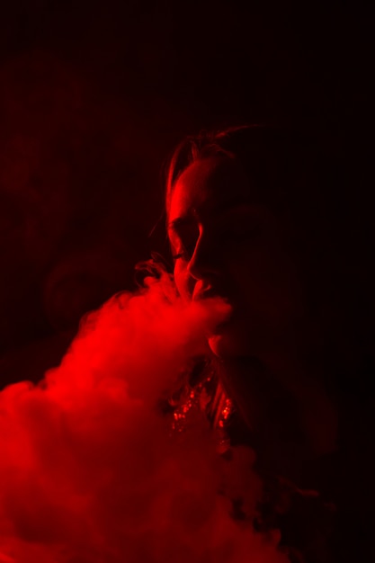 Girl model smokes vape in red light.