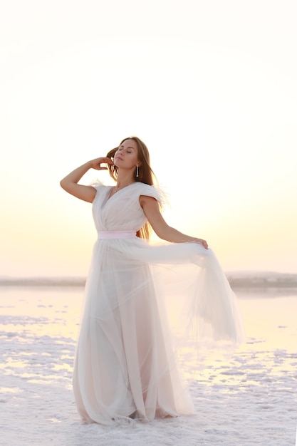 Modello di ragazza con lunghi capelli neri in abito lungo bianco sul lago salato
