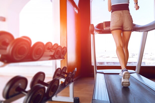 Girl on the morning run on the treadmill in the gym in front of a large window on the background of the sea