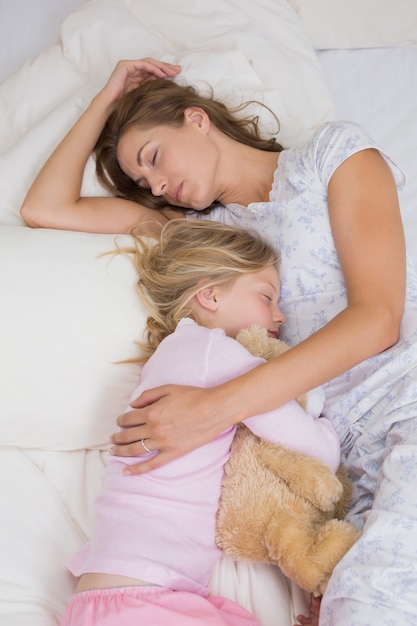 Girl and mother sleeping peacefully with stuffed toy in bed