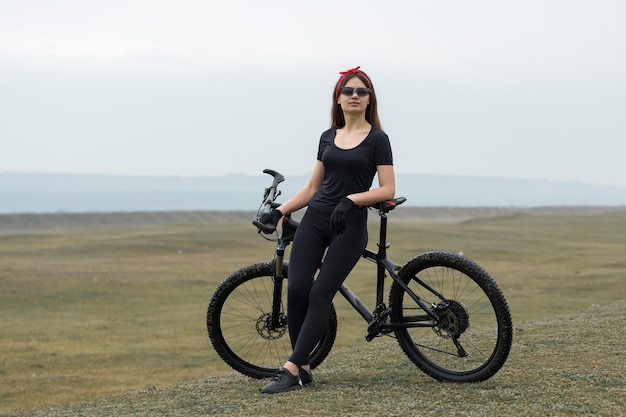 Girl on a mountain bike on offroad beautiful portrait of a\
cyclist in rainy weather fitness girl rides a modern carbon fiber\
mountain bike in sportswear closeup portrait of a girl in red\
bandana