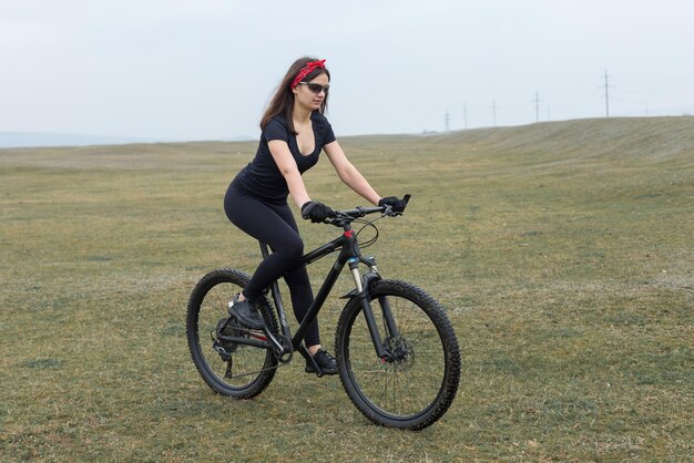 Girl on a mountain bike on offroad beautiful portrait of a
cyclist in rainy weather fitness girl rides a modern carbon fiber
mountain bike in sportswear closeup portrait of a girl in red
bandana