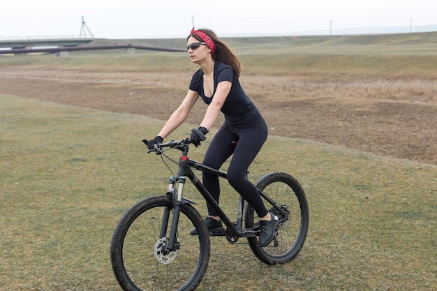 Girl on a mountain bike on offroad beautiful portrait of a\
cyclist in rainy weather fitness girl rides a modern carbon fiber\
mountain bike in sportswear closeup portrait of a girl in red\
bandana