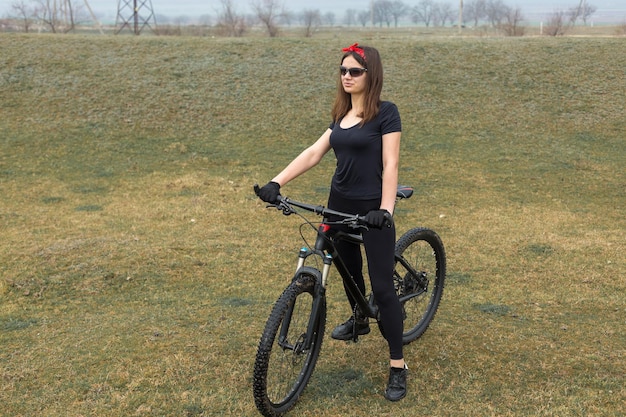 Girl on a mountain bike on offroad beautiful portrait of a\
cyclist in rainy weather fitness girl rides a modern carbon fiber\
mountain bike in sportswear closeup portrait of a girl in red\
bandana