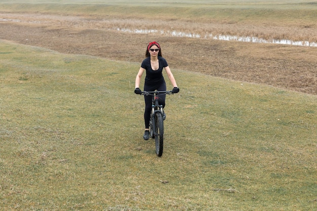 オフロードのマウンテンバイクの女の子日没時のサイクリストの美しい肖像画フィットネスの女の子がスポーツウェアでモダンなカーボンファイバーマウンテンバイクに乗るヘルメットとメガネの女の子のクローズアップの肖像画