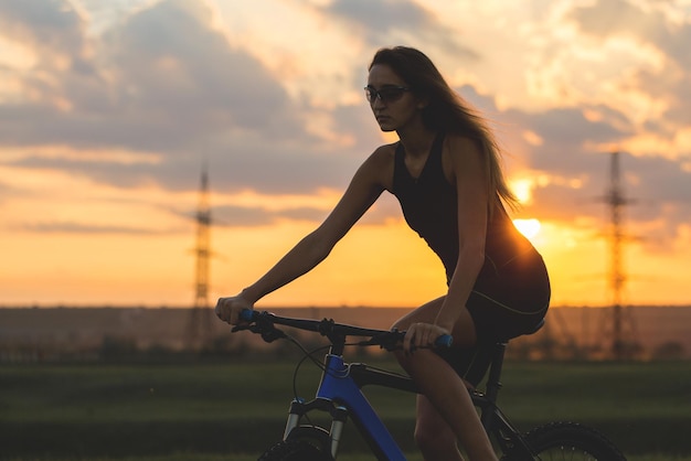 オフロードのマウンテンバイクの女の子日没時のサイクリストの美しい肖像画フィットネスの女の子がスポーツウェアでモダンな炭素繊維マウンテンバイクに乗るヘルメットとメガネの女の子のクローズアップの肖像画