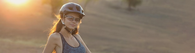 Girl on a mountain bike on offroad beautiful portrait of a cyclist at sunset Fitness girl rides a modern carbon fiber mountain bike in sportswear