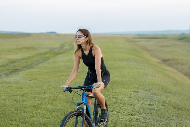 Ragazza in mountain bike in fuoristrada, bel ritratto di un ciclista al tramonto