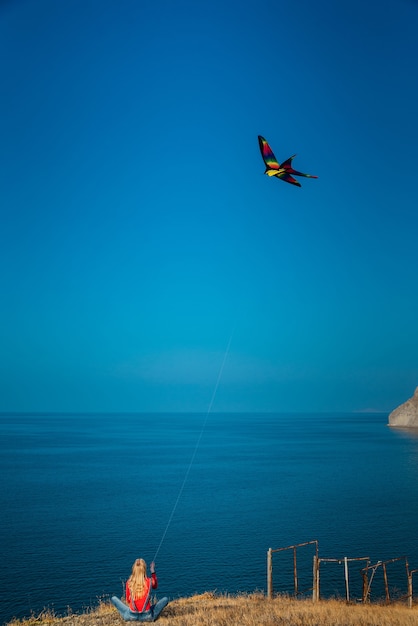 Girl on a mountainside by the sea launches a kite on a sunny day