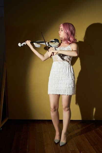 Girl musician with a violin in her hands in a stage dress. A woman with colored hair plays a modern violin