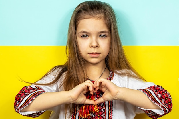 Photo a girl in national ukrainian clothes vyshyvanka shows a heart sign as a sign of love for ukraine