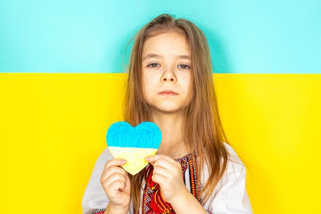 A girl in a national ukrainian vyshyvanka holds a heart painted in yellow and blue tones