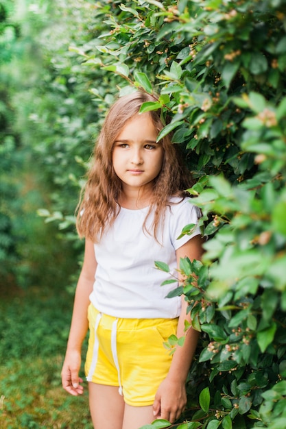 Girl near the bushes, green bushes, summer, walk, child, shorts, long hair, childhood