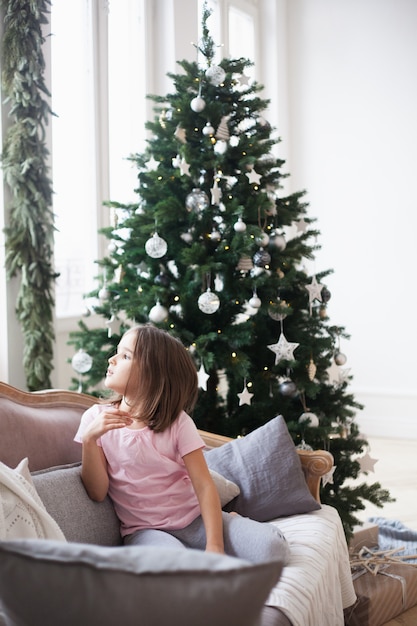 Girl near he Christmas tree, waiting for Santa Claus and a miracle