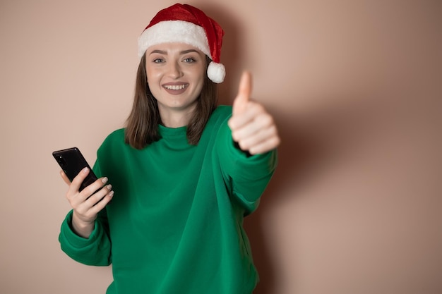 A girl in a New Year's hat is talking on the phone on a plain background holding a phone in her hand ordering dinner the concept of New Year's weekend 2023 happy christmas 2023 holidays