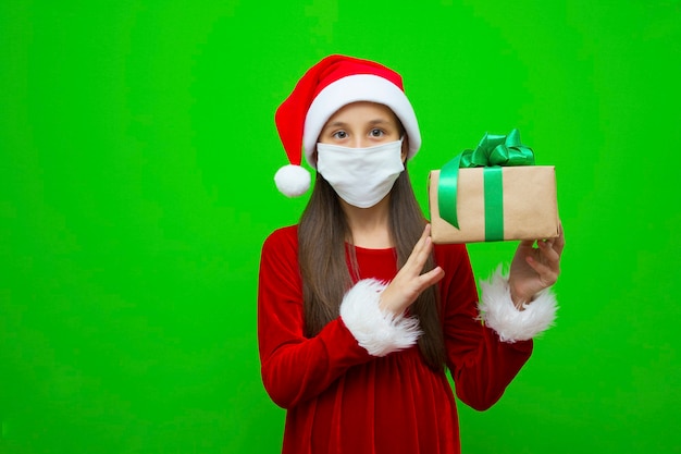 Girl in a new years cap in medical mask holds gift for christmas in hands place for advertising