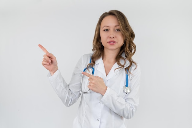 Девушка-медсестра в медицинском халате со стетоскопом на шее показывает знак руками
