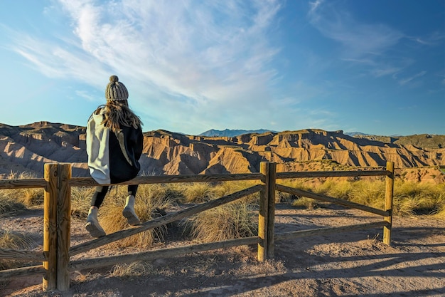 Girl observing the desert landscape leaning on a wooden fence