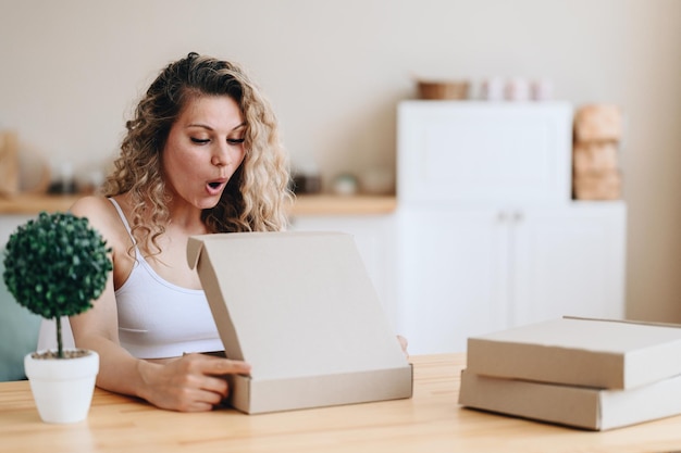 Girl opens her mouth in surprise looking into box girl holds Parcel in her hands Home delivery