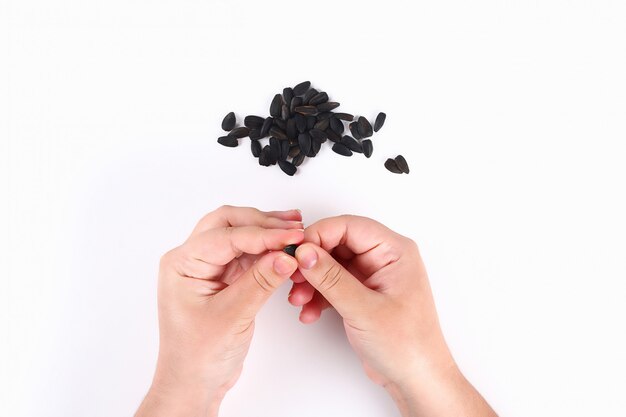 The girl opens sunflower seeds with her hands on white. Top view.