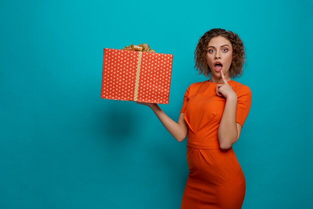 Girl in orange dress holding red box with bow.