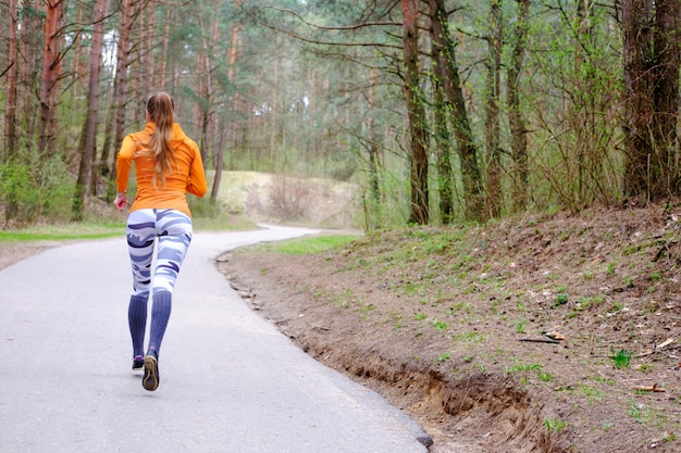 Foto ragazza in felpa con cappuccio arancione eseguita nella foresta