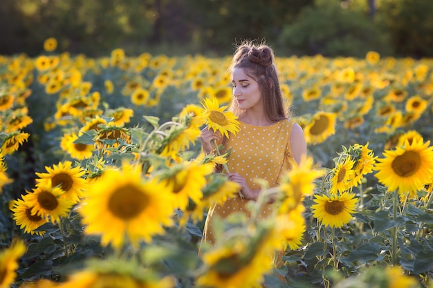 해질녘 여름에 해바라기 밭에서 오렌지 빛 sundress에 소녀.