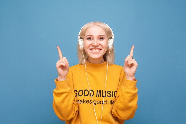 주황색 셔츠를 입은 소녀는 헤드폰에서 음악을 듣고 손가락을 보여줍니다.