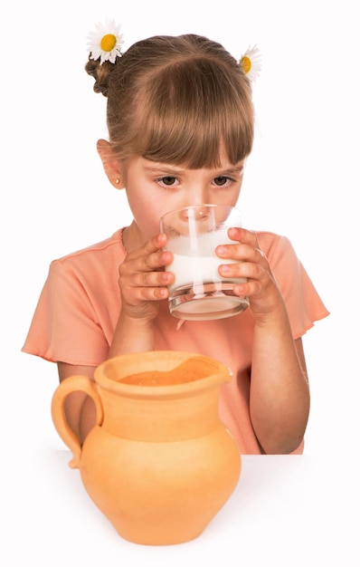 Girl in an orange Tshirt and flowers in her hair drinks fresh milk on a white background